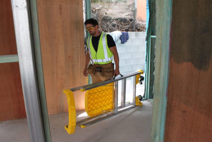 Bailey P170 Job Station Aluminium Platform Ladder man with high vis top, safety glasses carrying ladder using handle