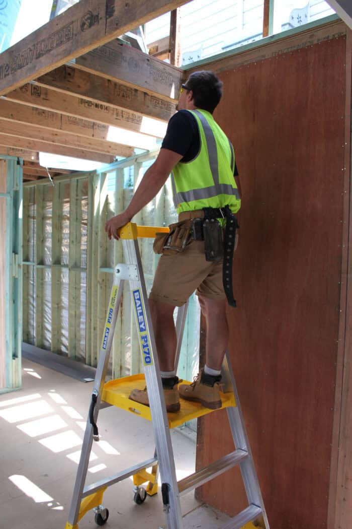 Bailey P170 Job Station Aluminium Platform Ladder FS13538, man in high-vis and tool belt on yellow platform holding safety rail, inspecting building beams